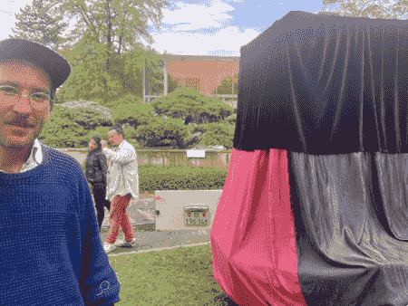 selfie d'un artiste avec deux artistes qui marchent derrière et la Boîte à Rêves sur le côtế