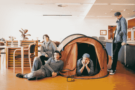 quatre artistes posent autour d'une tente de camping dans une cafétéria