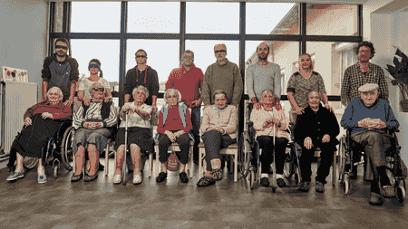 huit personnes agées assises et hui personnes debout derrière, dont cinq avec les yeux bandés